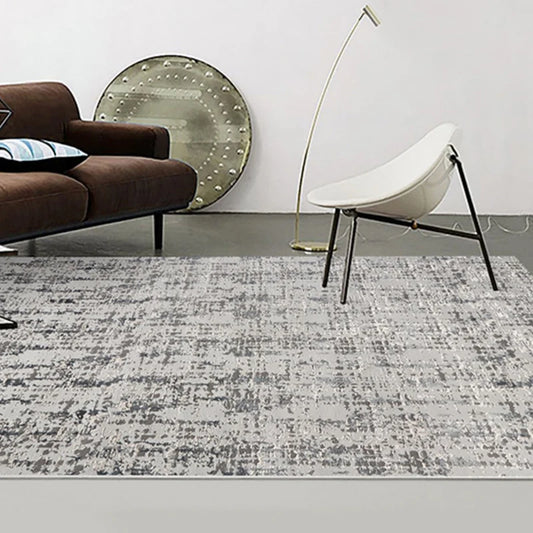 Modern living room with a textured abstract gray area rug, featuring a brown sofa, a sleek white chair, and minimalistic decor.