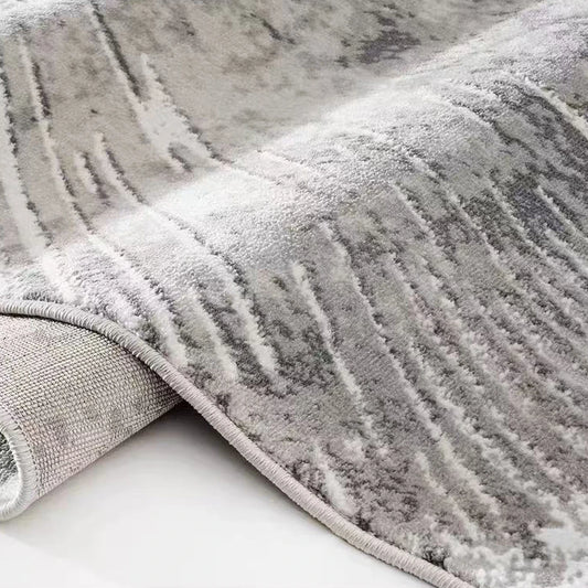 Grey abstract burst area rug shown in a rolled close-up with soft textured pile and reinforced edge