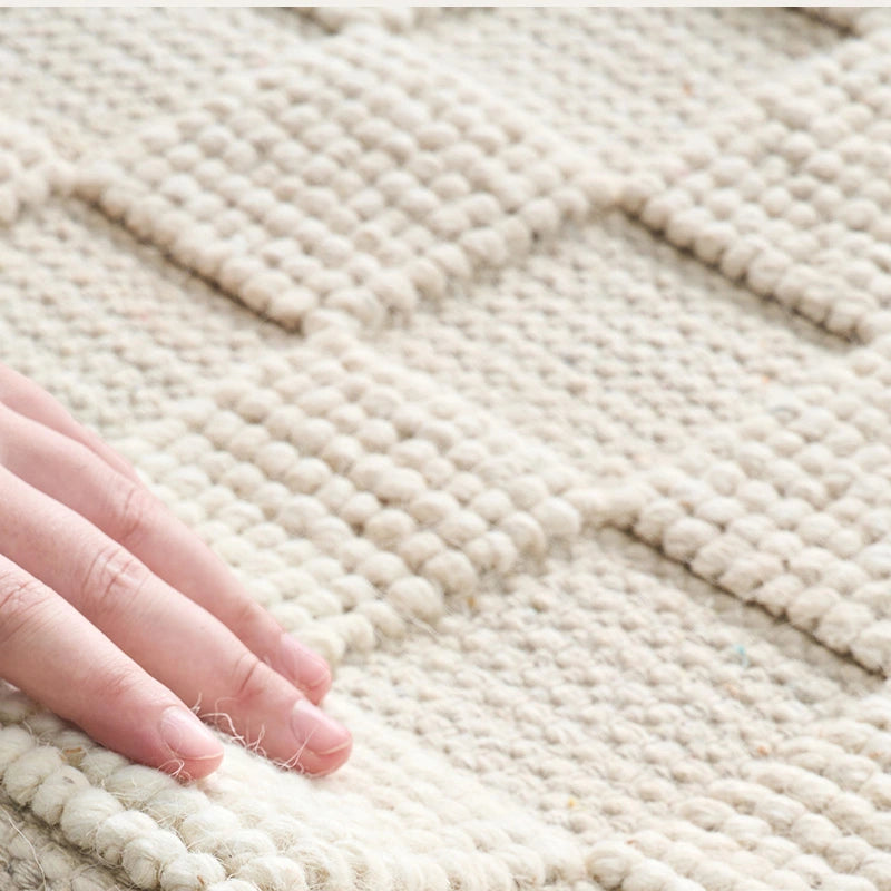 A handwoven wool rug with natural texture being gently touched, highlighting its soft and intricate craftsmanship #color_Beige Texture
