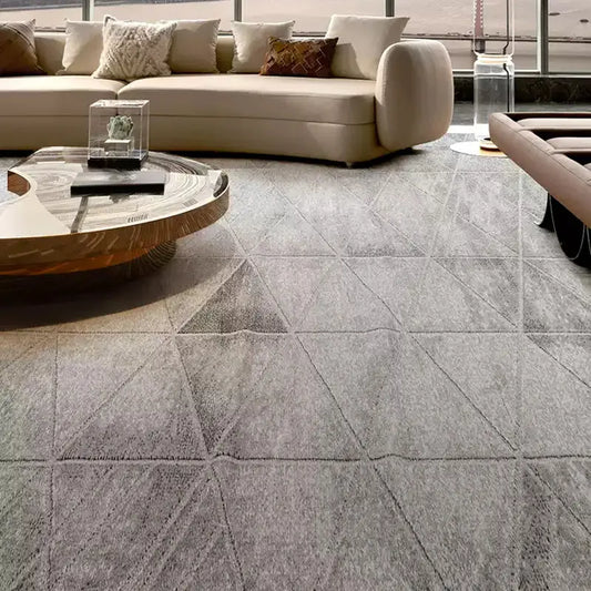 Modern living room featuring a grey geometric-patterned rug, curved beige sofa, artistic wooden coffee table, and luxury decor elements