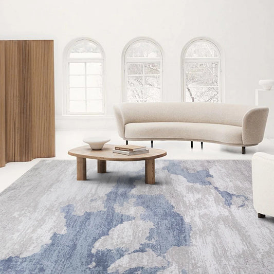 Living room with a blue-gray abstract rug, curved beige sofa, and wood accents creating a serene atmosphere  #color_blue