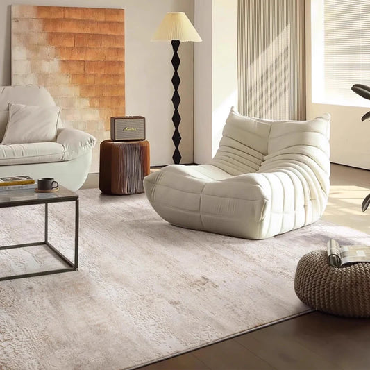 A modern minimalist living room with a soft area rug, a cozy white lounge chair, and natural light filling the space