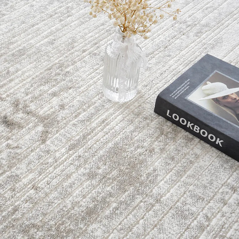 Close-up of a neutral abstract rug with textured patterns, a glass vase with flowers, and a lookbook #color_gray