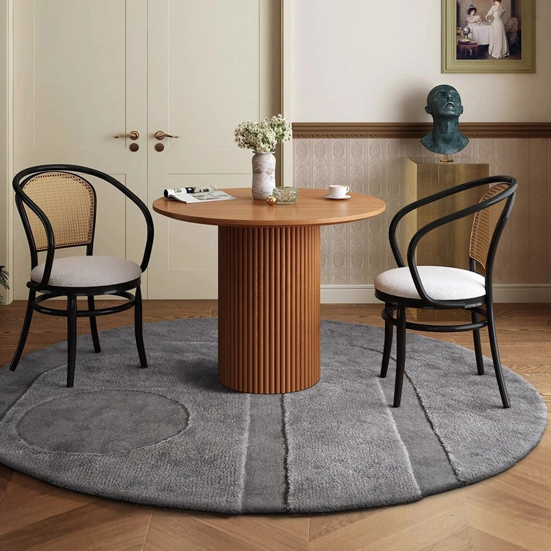 Round gray rug under a wooden dining table with two black chairs in a cozy dining area #Shape_Round