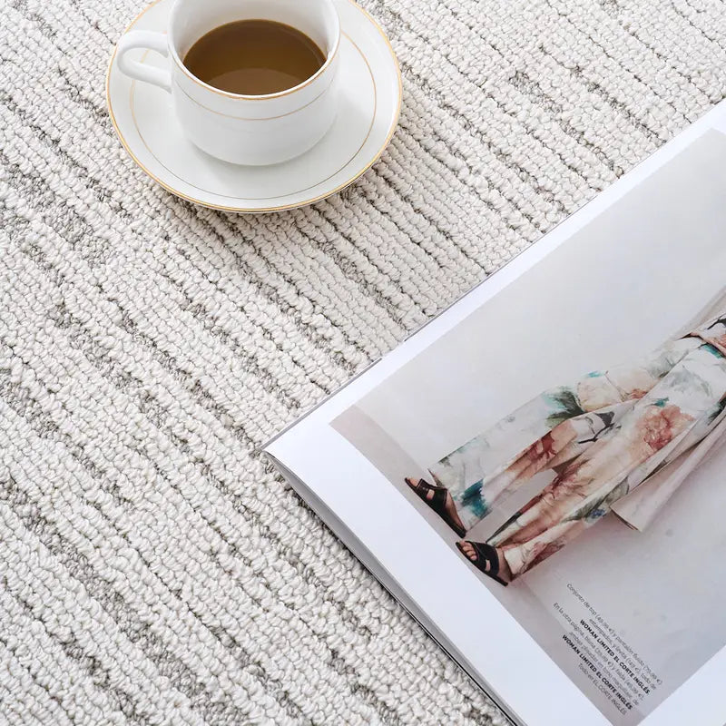 Close-up of a neutral striped rug with a coffee cup and magazine, highlighting soft woven texture  #Texture_Stripe