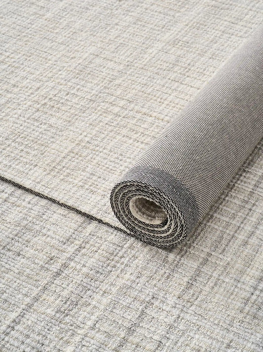 Close-up of a rolled neutral wool-blend area rug showcasing its textured weave and natural backing