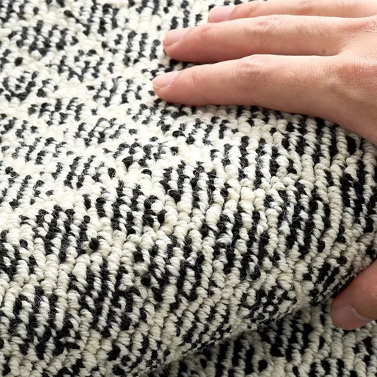 Close-up of a hand touching a soft area rug with high-low loop texture and black-and-white woven pattern