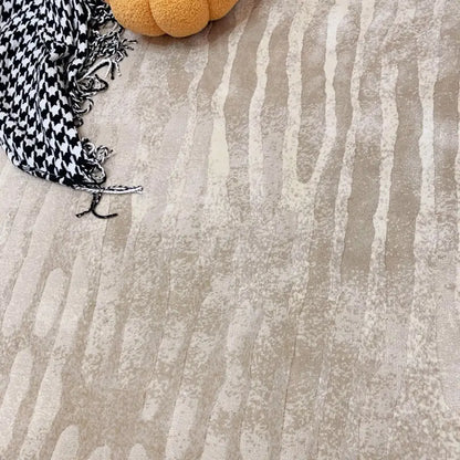 Close-up detail of beige abstract wave-patterned area rug, showcasing soft texture and subtle color variations, with decorative accessories