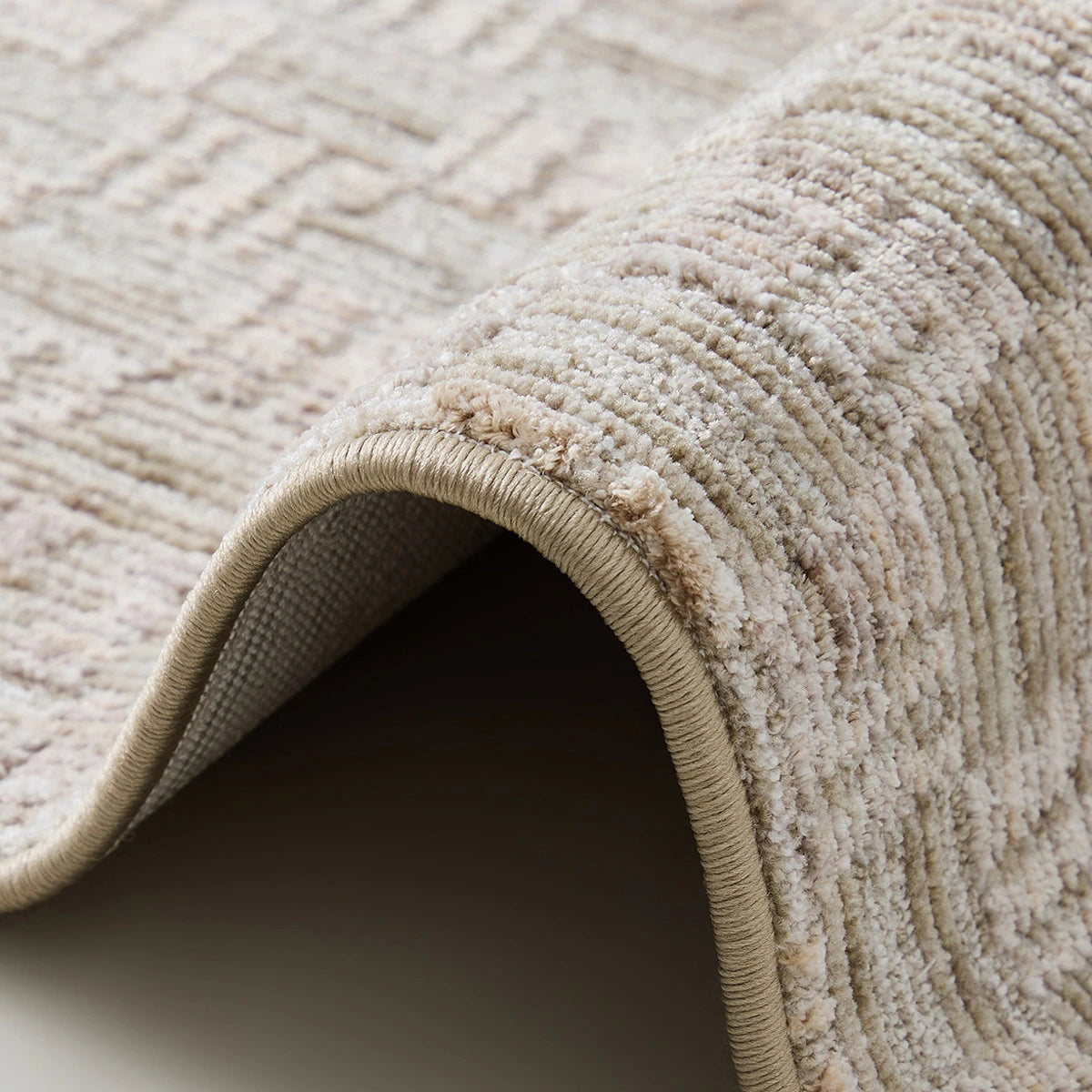 Beige crosshatch woven rug edge showing reinforced binding and a thick textured surface