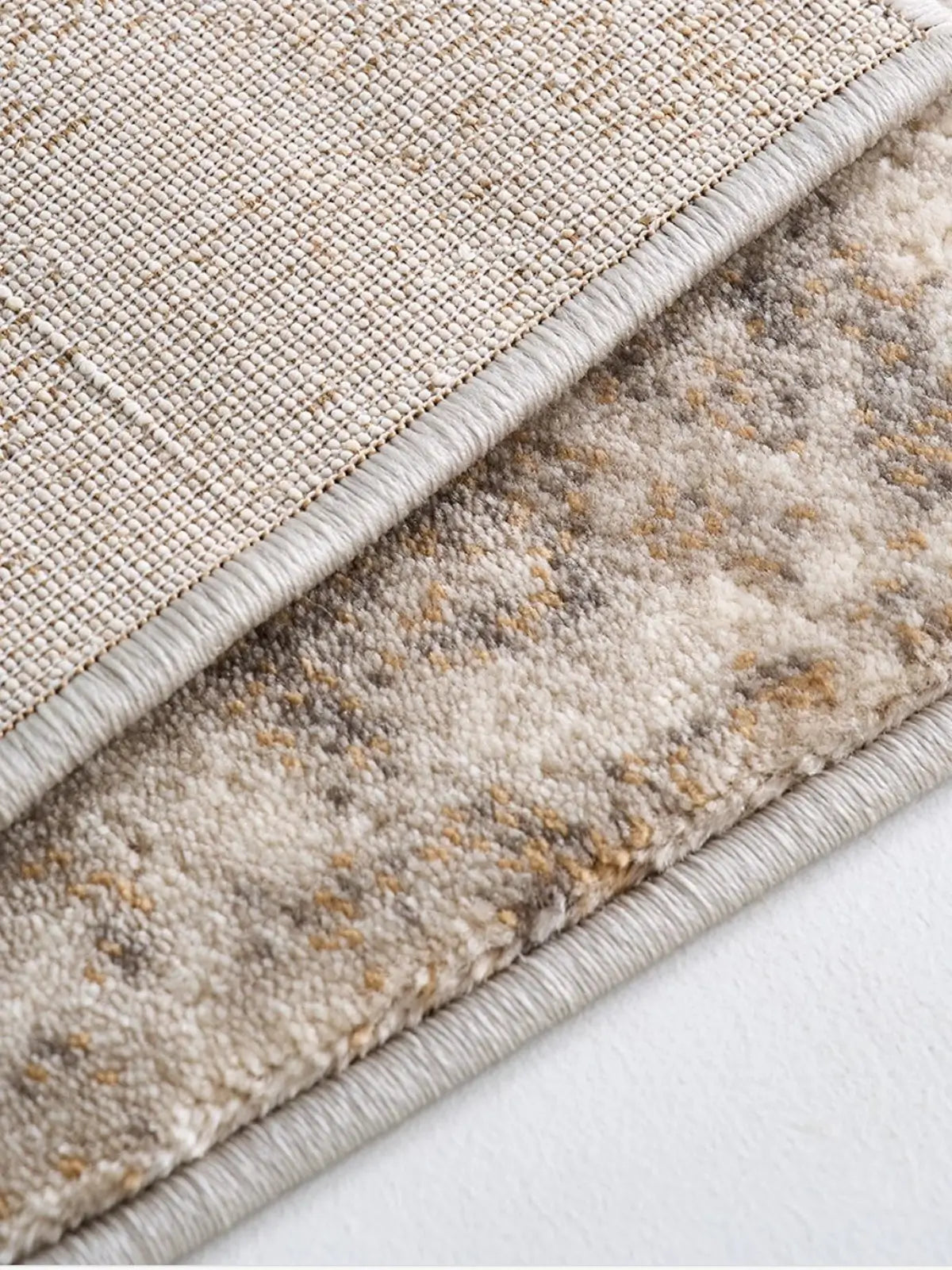 Close-up of a beige rug showcasing its backing texture and neatly stitched edge