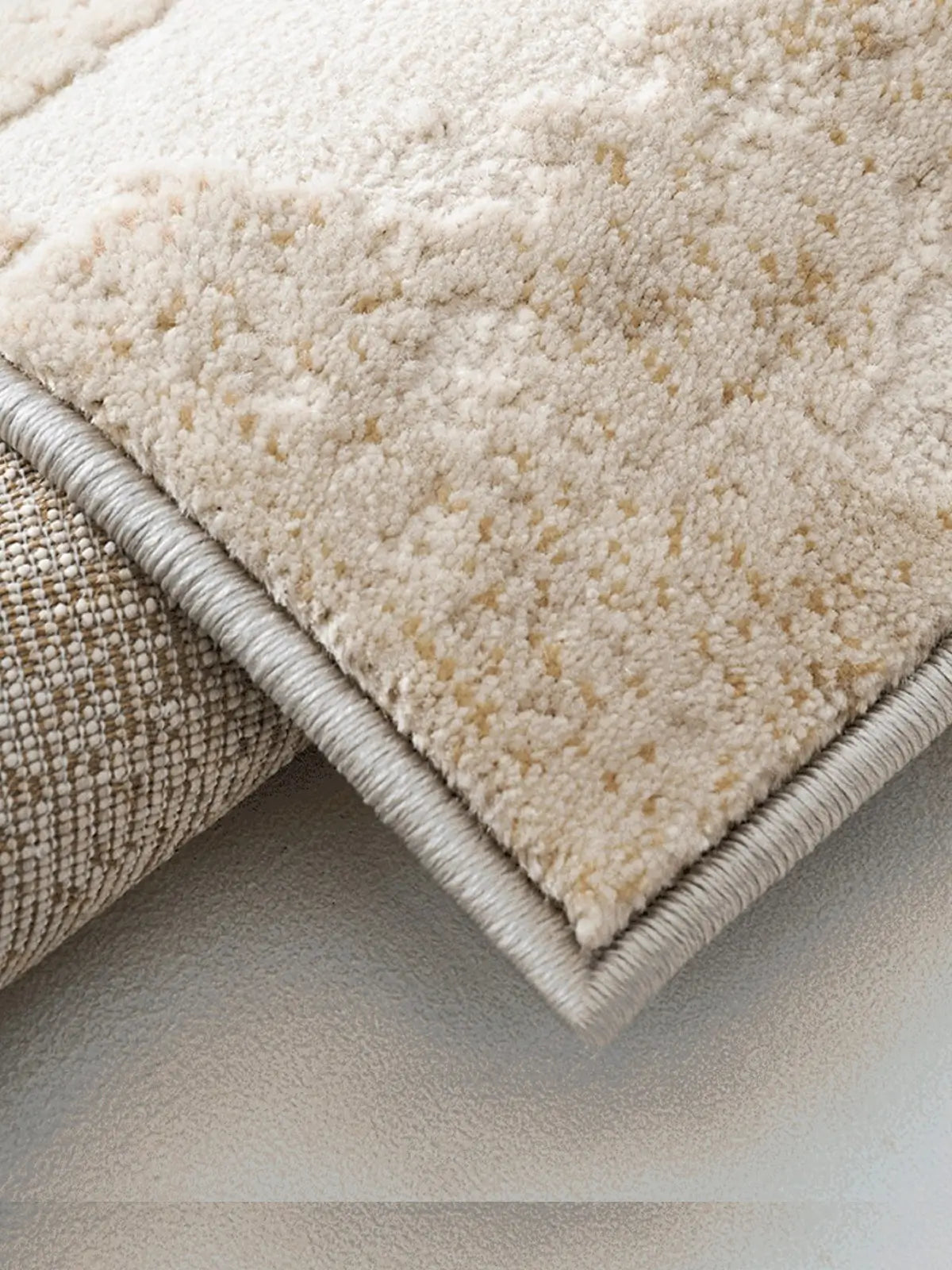 Detailed view of the edge of a beige rug showing its stitching and layered texture
