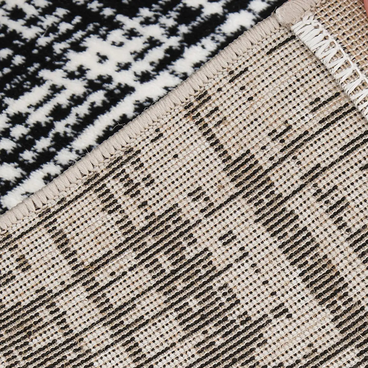 Backing detail of a black and white abstract border area rug showing the woven backing and reinforced bound edge.