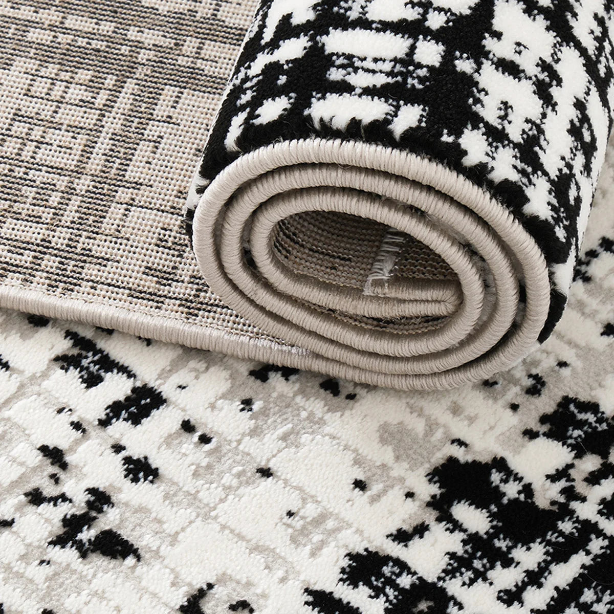 Close-up of a black and white abstract border area rug showing the rolled edge, bound finish, and woven backing.