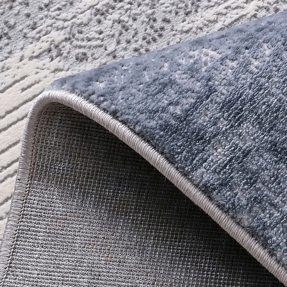 Blue-gray abstract area rug backing and bound edge detail showing the woven underside, finished edge, and thick rug construction.