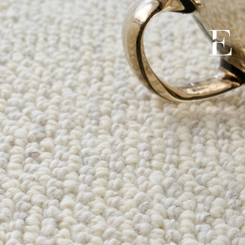 Close-up view of a loop-pile wool rug showing its dense texture and soft hand-feel, paired with a golden cup.