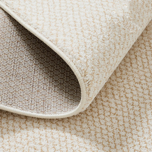 Close up of cream beige rug edge showing bound edges, soft pile, and woven backing