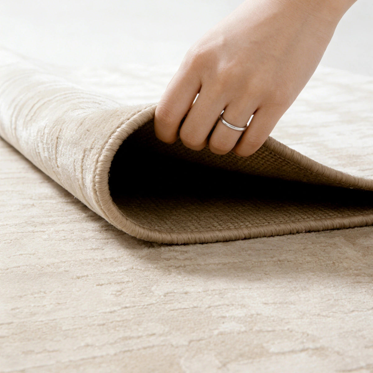 soft cream area rug being lifted to show flexible edge and comfortable thickness