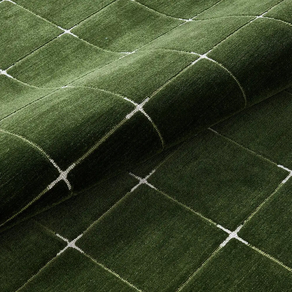 Rolled edge detail of a green grid area rug showing thick dense pile.