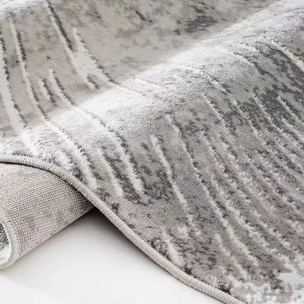 Grey abstract burst area rug shown in a rolled close-up with soft textured pile and reinforced edge