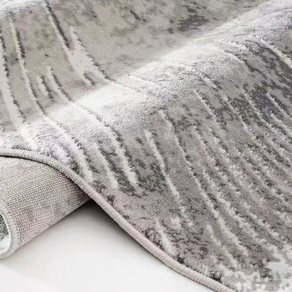 Grey abstract burst area rug shown in a rolled close-up with soft textured pile and reinforced edge