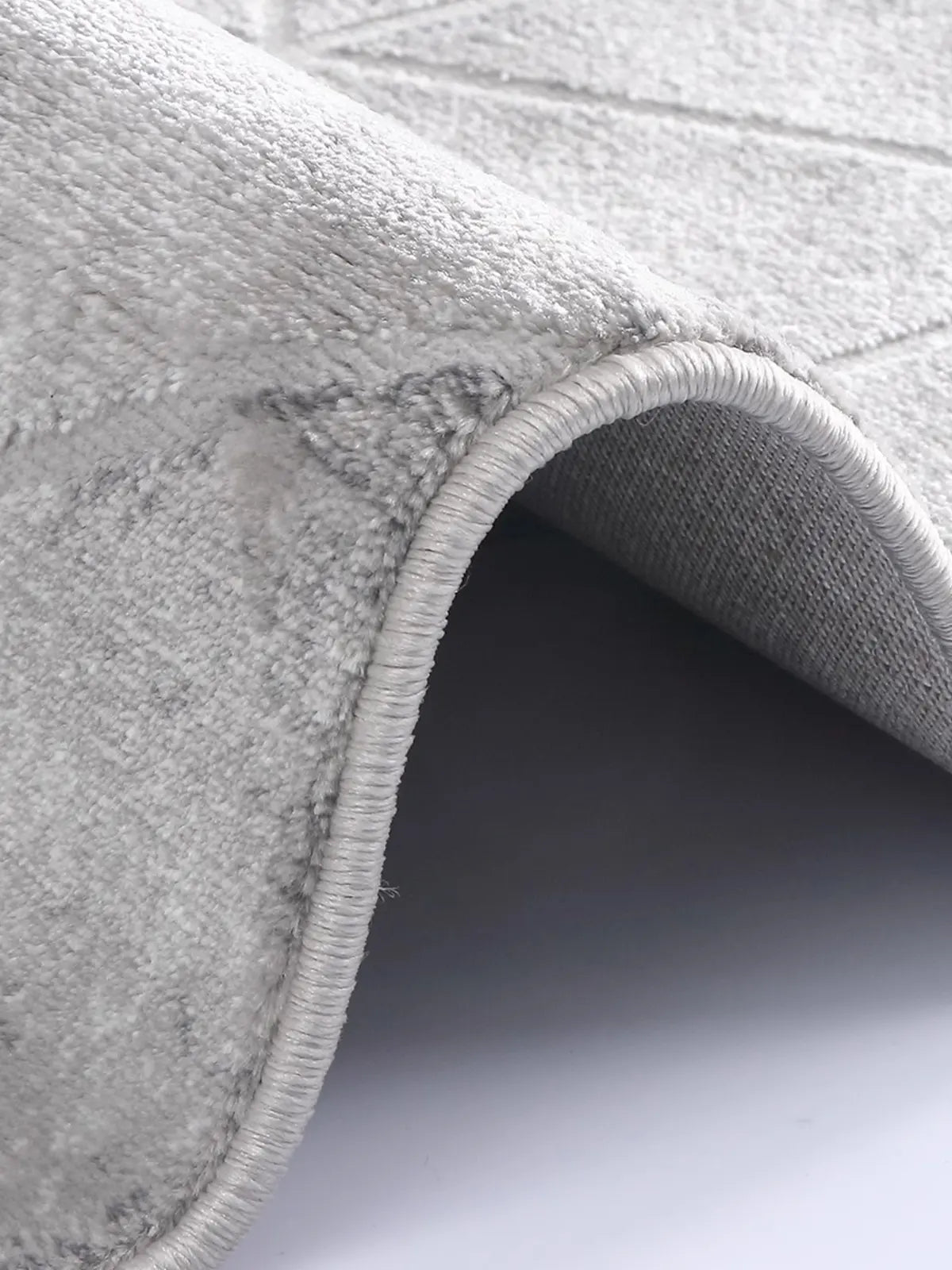 Close-up of grey geometric-patterned rug showcasing soft plush texture, reinforced stitched edges, and premium craftsmanship