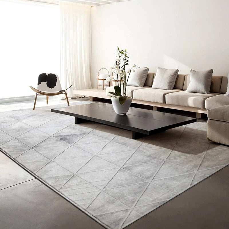 Modern minimalist living room featuring a grey geometric-patterned rug, neutral-toned furniture, low-profile coffee table, and soft natural lighting