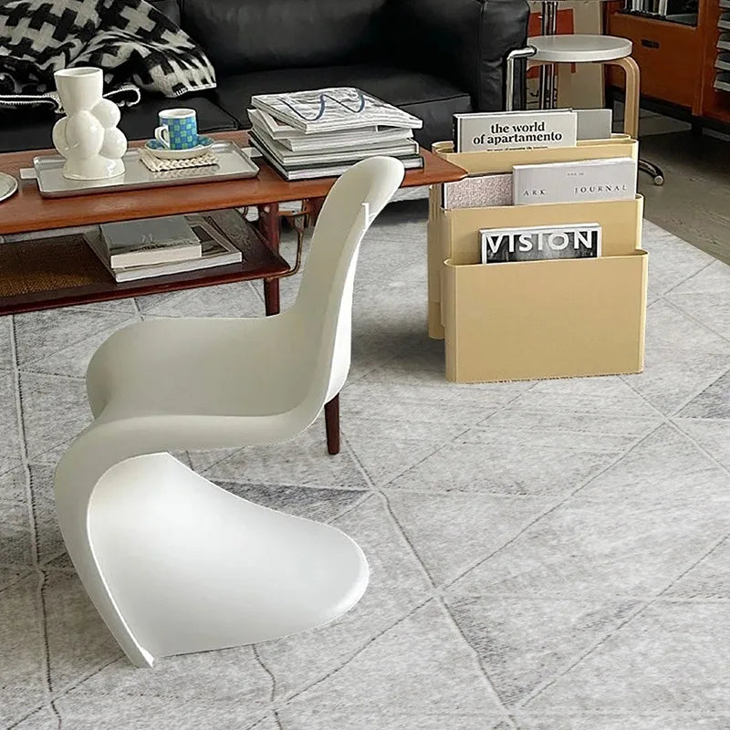 Modern vintage living space featuring a grey geometric-patterned rug, sculptural white chair, wooden coffee table, and stylish magazine storage