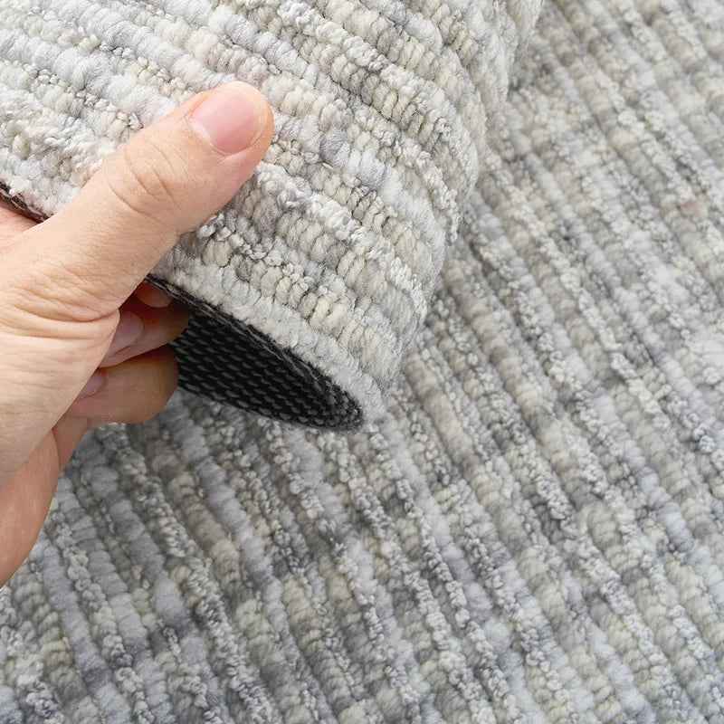 Hand holding a thick loop-pile wool blend rug in soft grey tones, showing detailed craftsmanship.