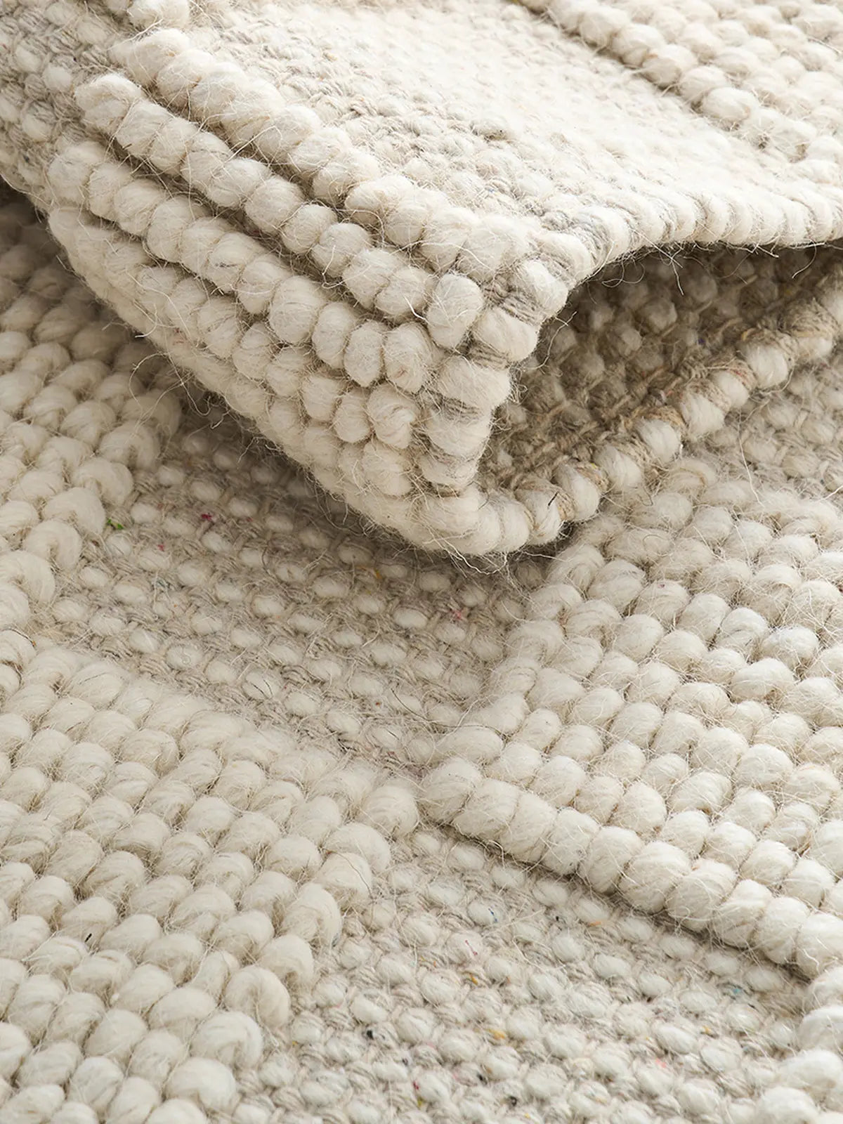 Close-up of a folded handwoven wool rug showing intricate texture and craftsmanship, natural beige tones