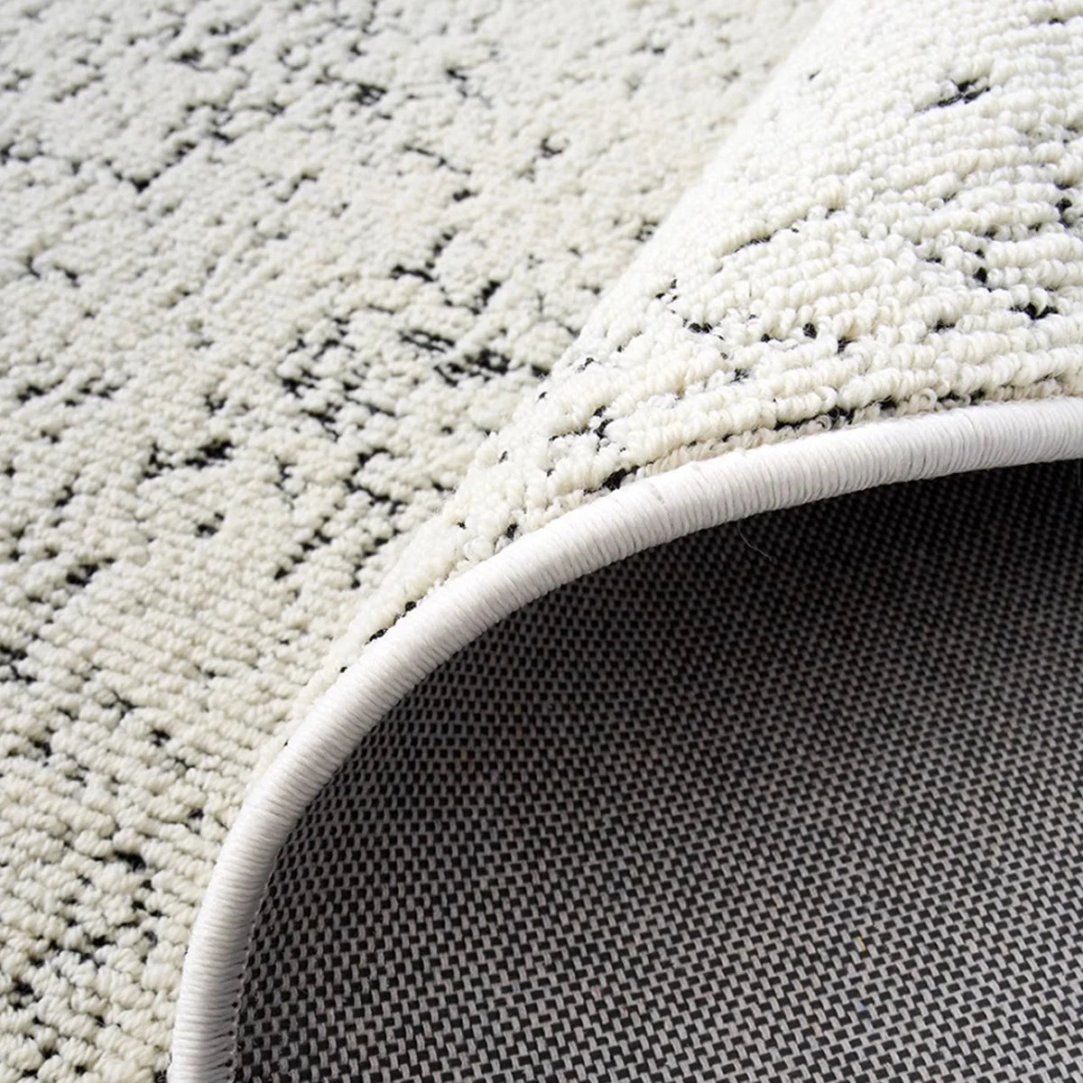 Close-up edge detail of an ivory black textured rug with dense woven construction and flexible backing