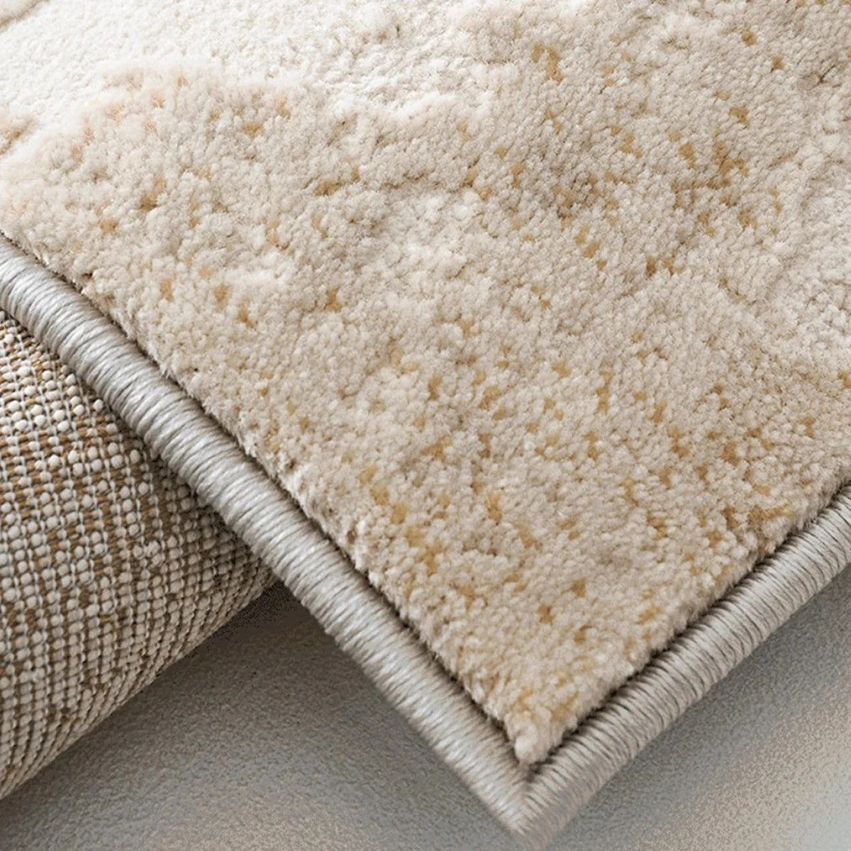 Folded corner detail of an ivory and gray abstract distressed area rug showing the woven backing and bound edge.
