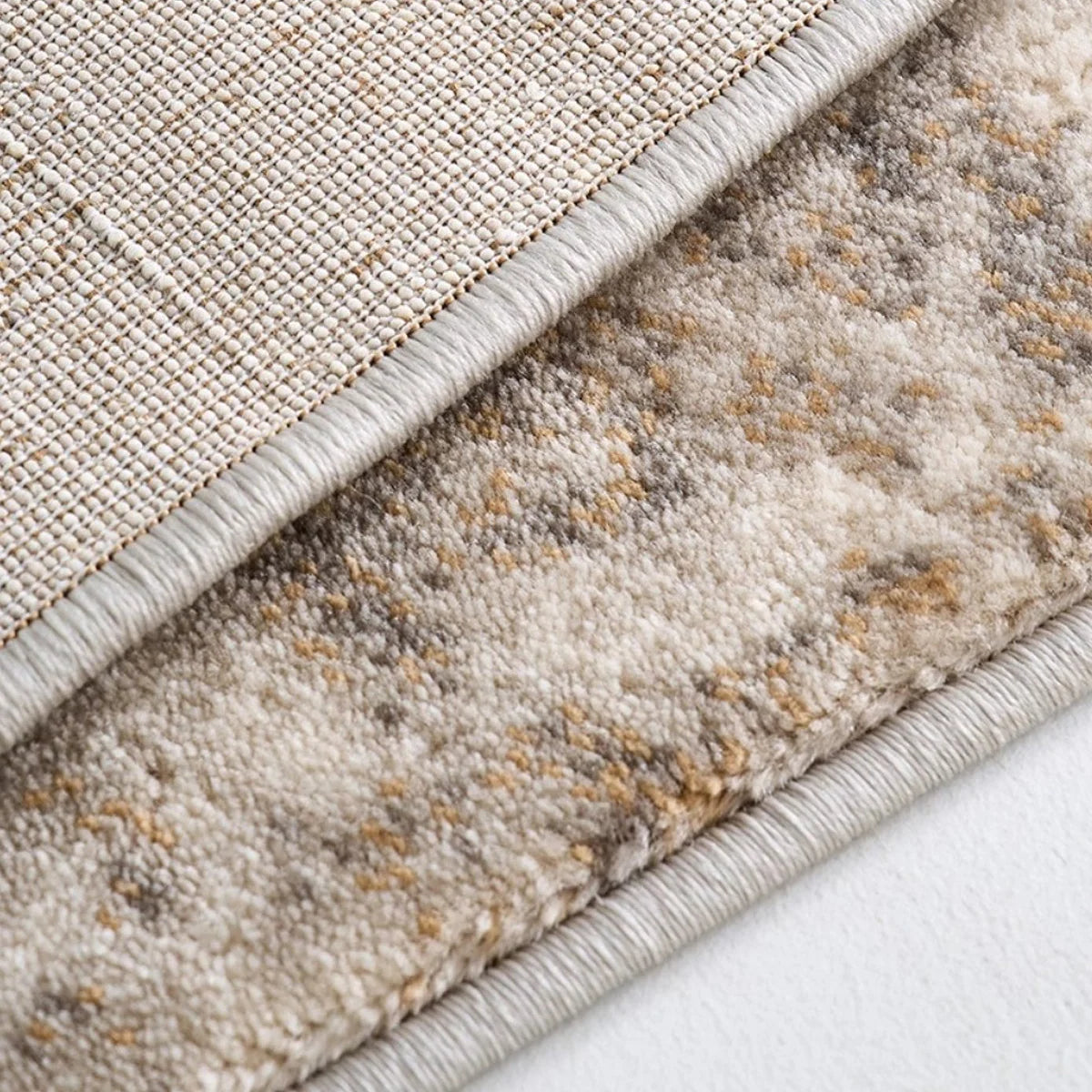 Folded back view of an ivory and gray abstract distressed rug showing the backing, edge finish, and soft patterned surface.