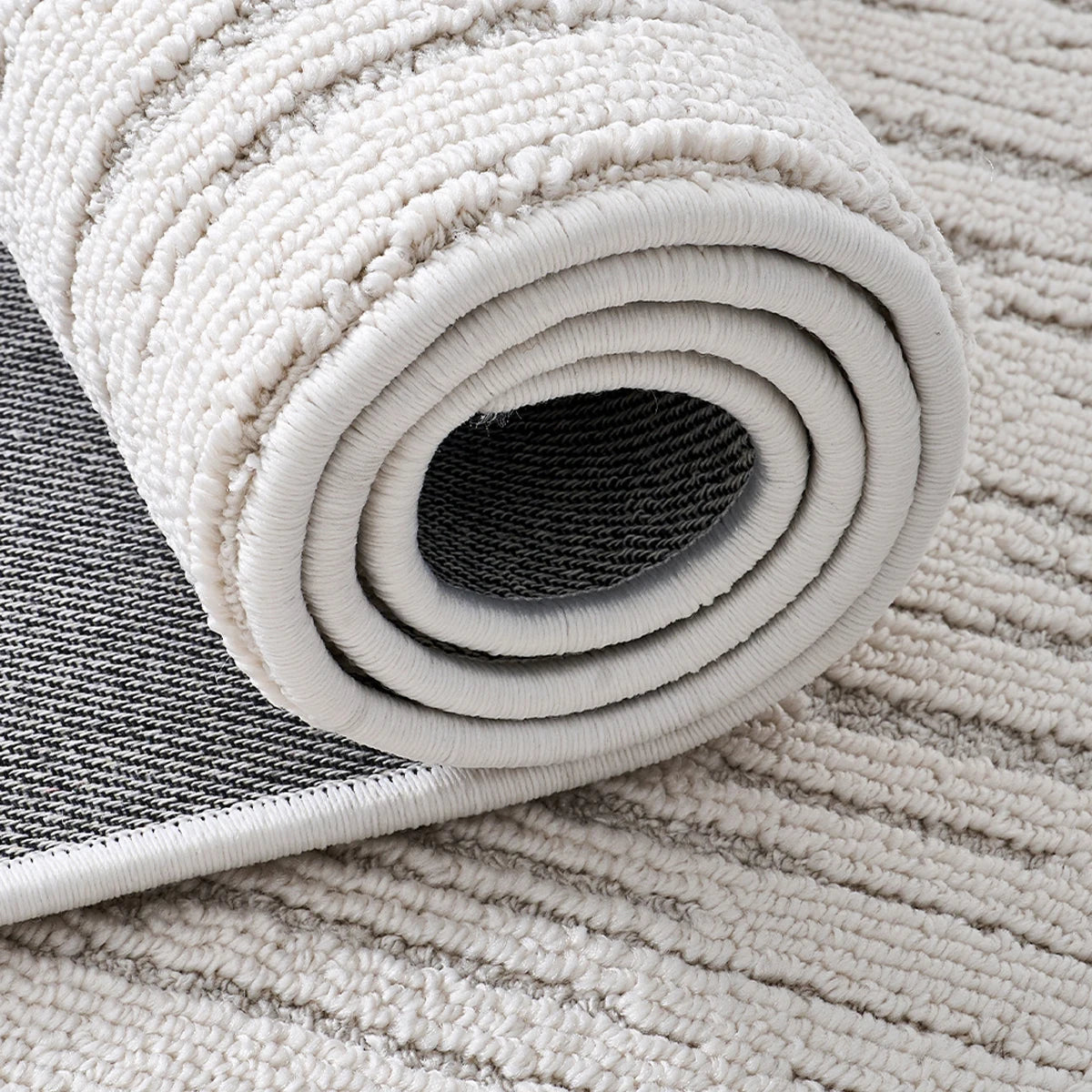 Ivory textured area rug rolled up to show flexible construction and finished edges