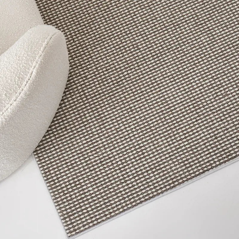 Close-up of wool blend loop rug in cream and taupe, paired with a boucle armchair on white floor