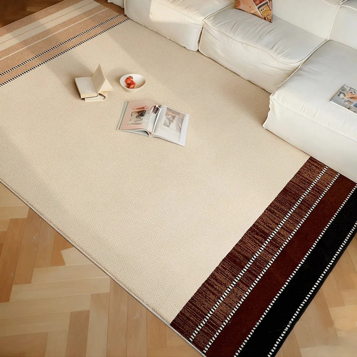 Cream beige border rug with warm brown and black striped edges beside a white sofa