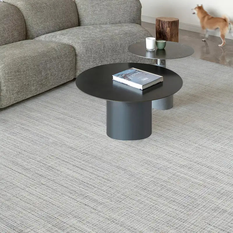 Minimalist wool-blend area rug in light grey tones, styled with a modern grey sofa and round black coffee tables.