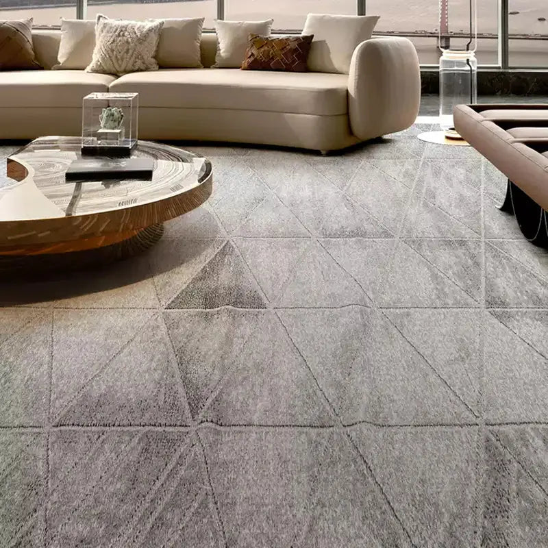 Modern living room featuring a grey geometric-patterned rug, curved beige sofa, artistic wooden coffee table, and luxury decor elements