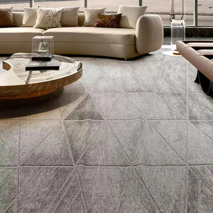 Modern living room featuring a grey geometric-patterned rug, curved beige sofa, artistic wooden coffee table, and luxury decor elements