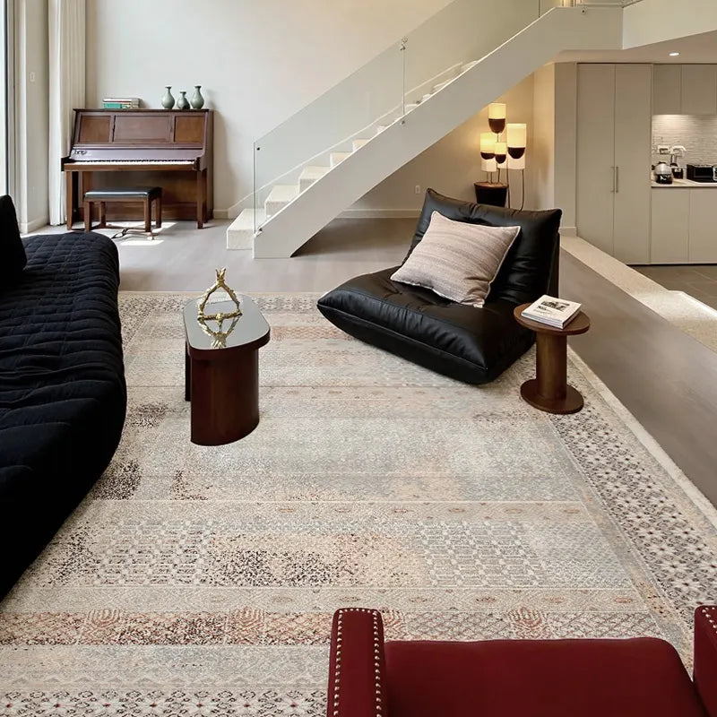 Modern minimalist living space featuring a gray vintage area rug, low black sofa, and wooden accent tables