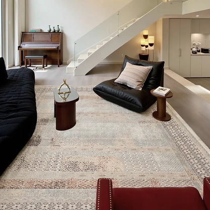 Modern minimalist living space featuring a gray vintage area rug, low black sofa, and wooden accent tables