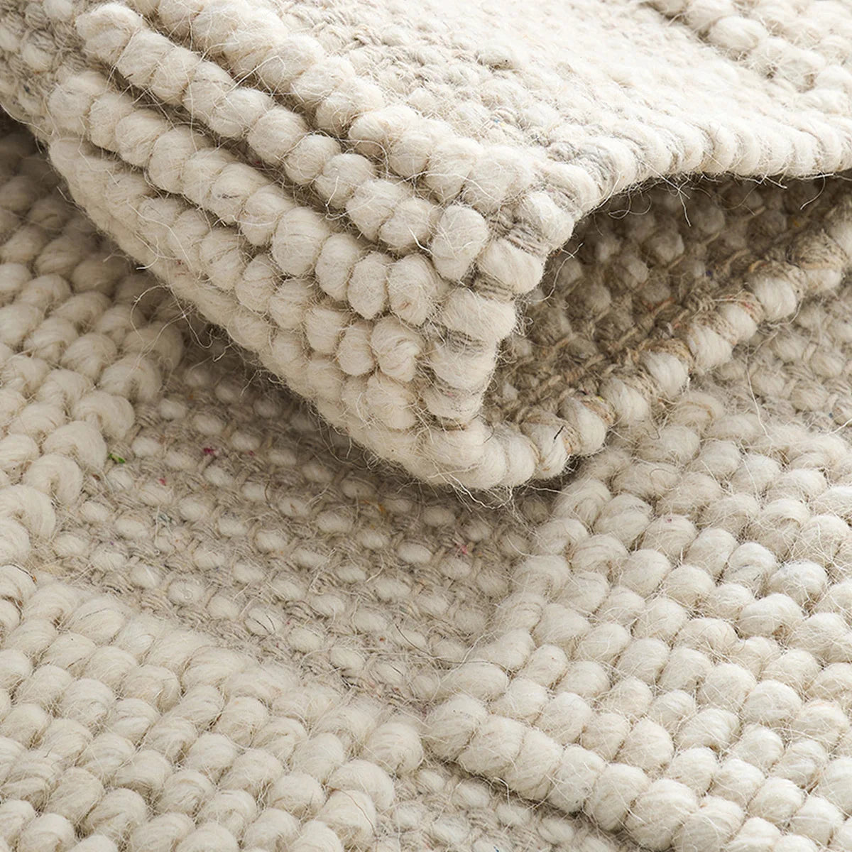 Natural ivory handwoven wool area rug folded detail showing thick chunky wool texture and raised woven pile.