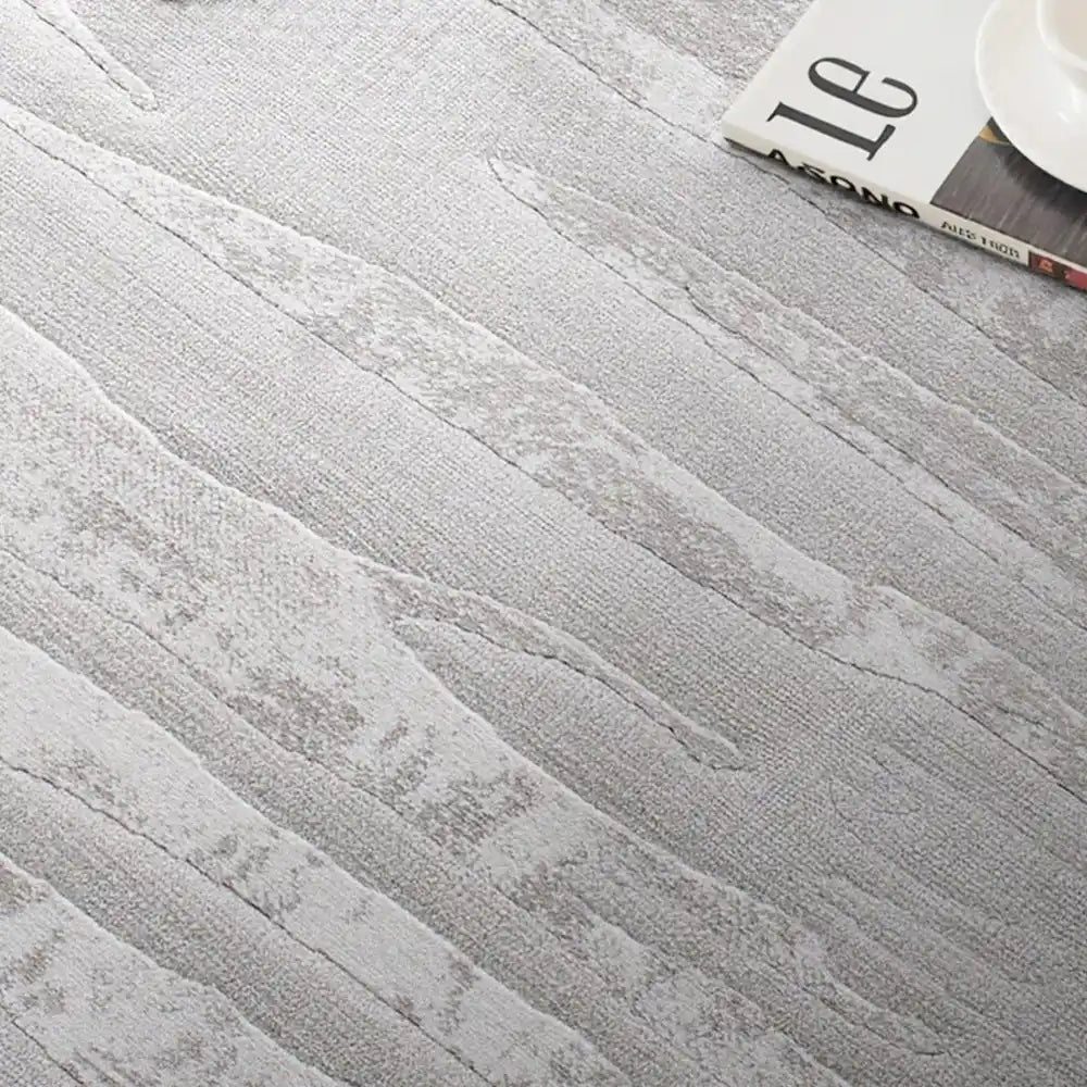 Neutral gray textured rug detail in a minimalist bedroom setting with books and soft natural light