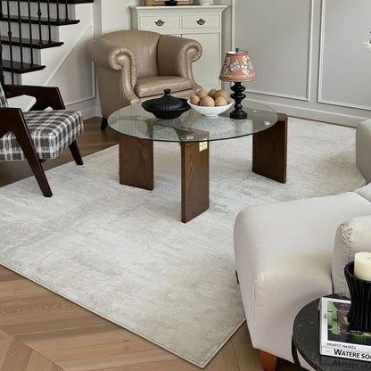 A neutral-toned modern rug anchors a refined living room setup with mixed textures—glass, wood, leather, and fabric—blending timeless elegance with everyday comfort