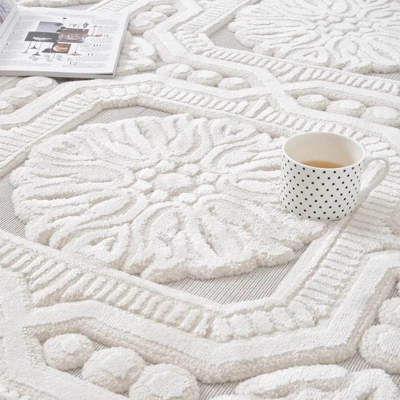 A detailed close-up of an ivory sculpted floral-patterned rug, featuring a polka-dotted coffee mug placed on its textured surface, adding a cozy and elegant touch to the scene #Series_Classic Relief
