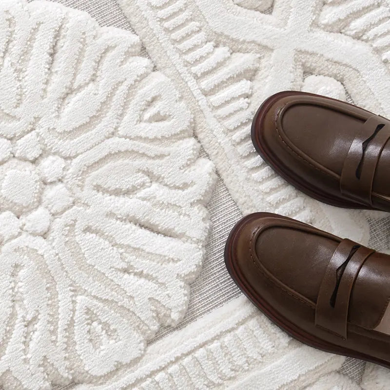 A close-up of a sculpted floral-patterned rug in soft ivory tones, paired with elegant brown leather loafers, highlighting the rug's intricate texture and luxury appeal #Series_Classic Relief