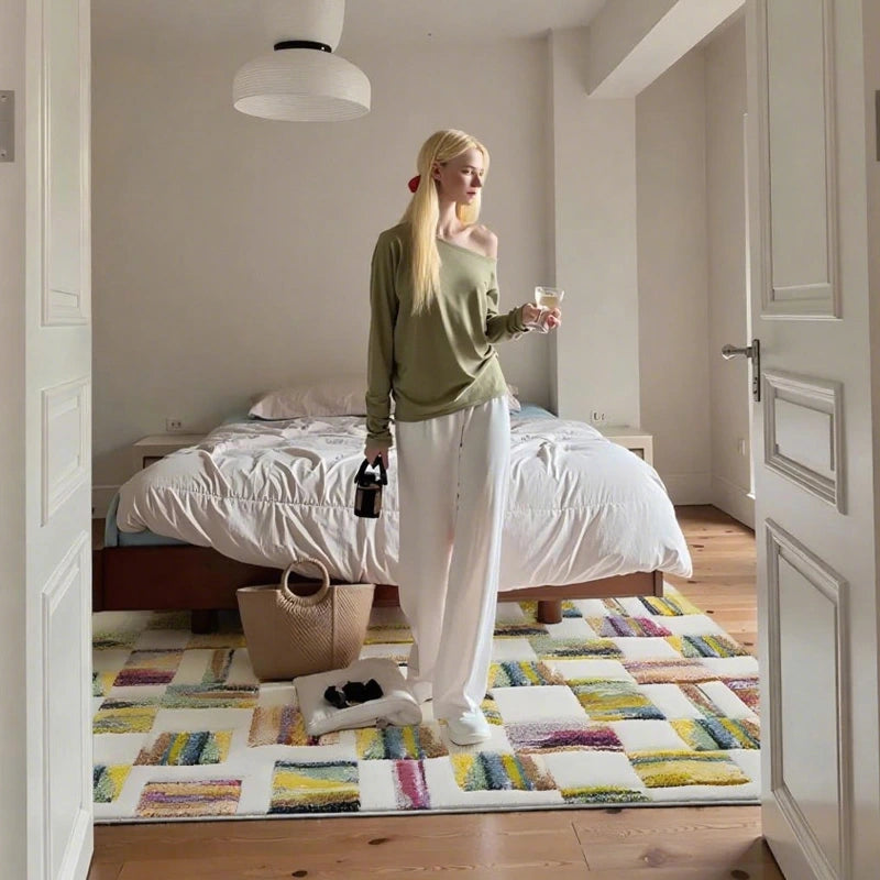 Colorful patchwork rug in a bright minimalist bedroom with a woman standing by the bed holding a drink
