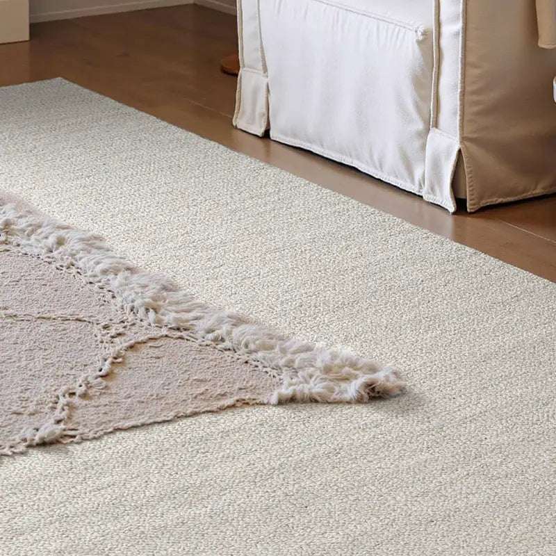 Natural wool rug in light beige tones with textured weave, styled in a cozy living room with layered fabric and soft sunlight.