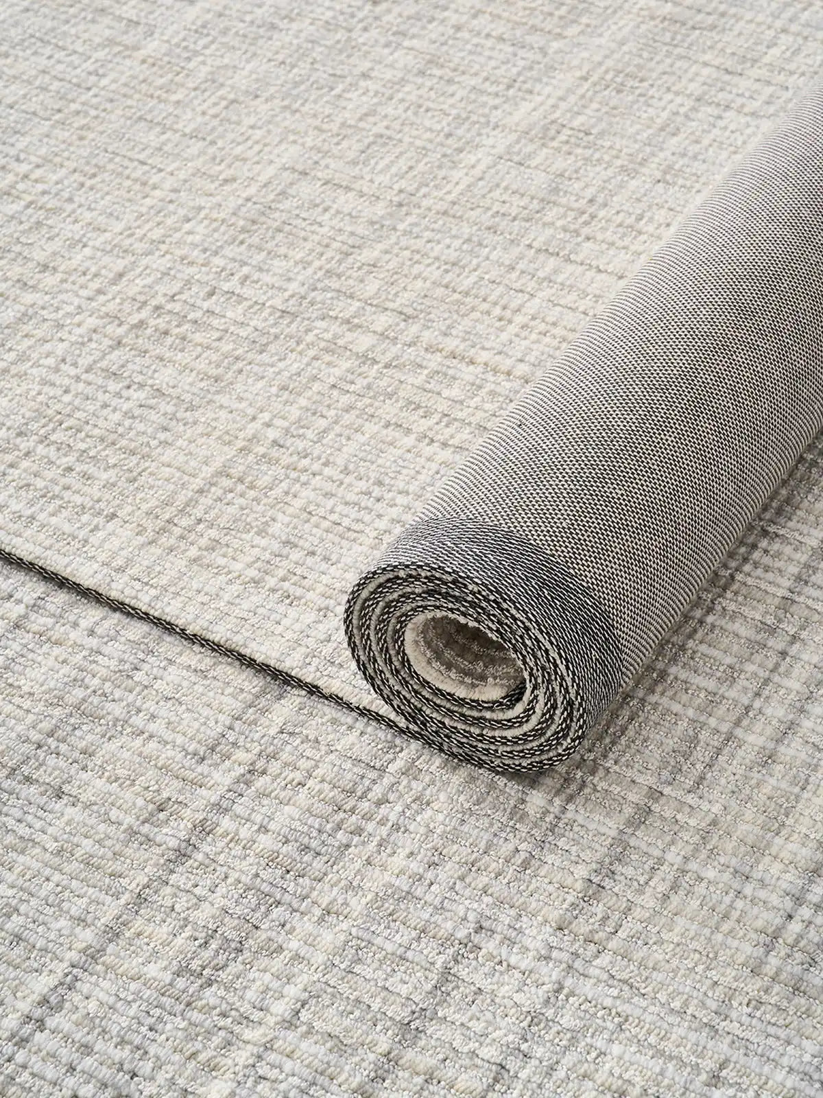 Close-up of a rolled neutral wool-blend area rug showcasing its textured weave and natural backing
