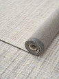 Close-up of a rolled neutral wool-blend area rug showcasing its textured weave and natural backing