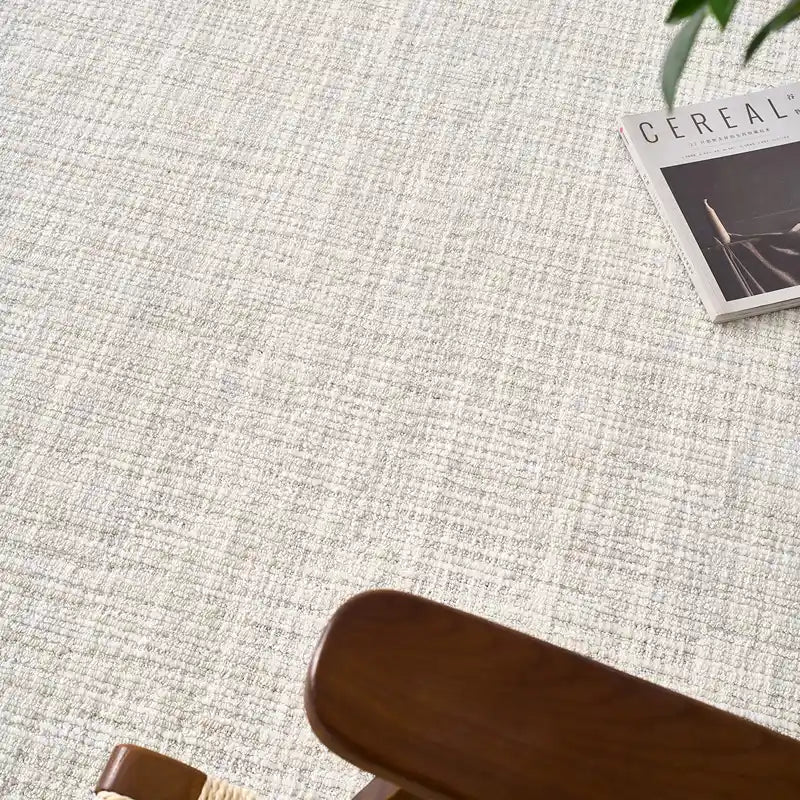 Close-up of a neutral textured wool blend rug with a wooden chair and a lifestyle magazine on top